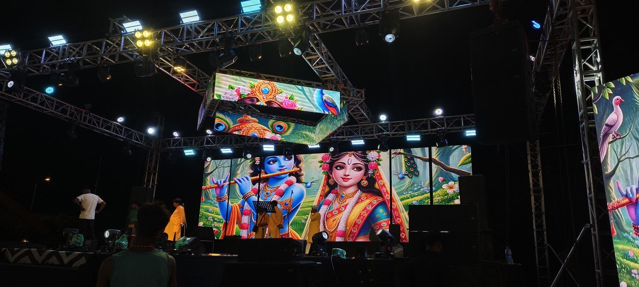 Crew setting up in front of a bright outdoor LED screen on a truss stage before an evening show