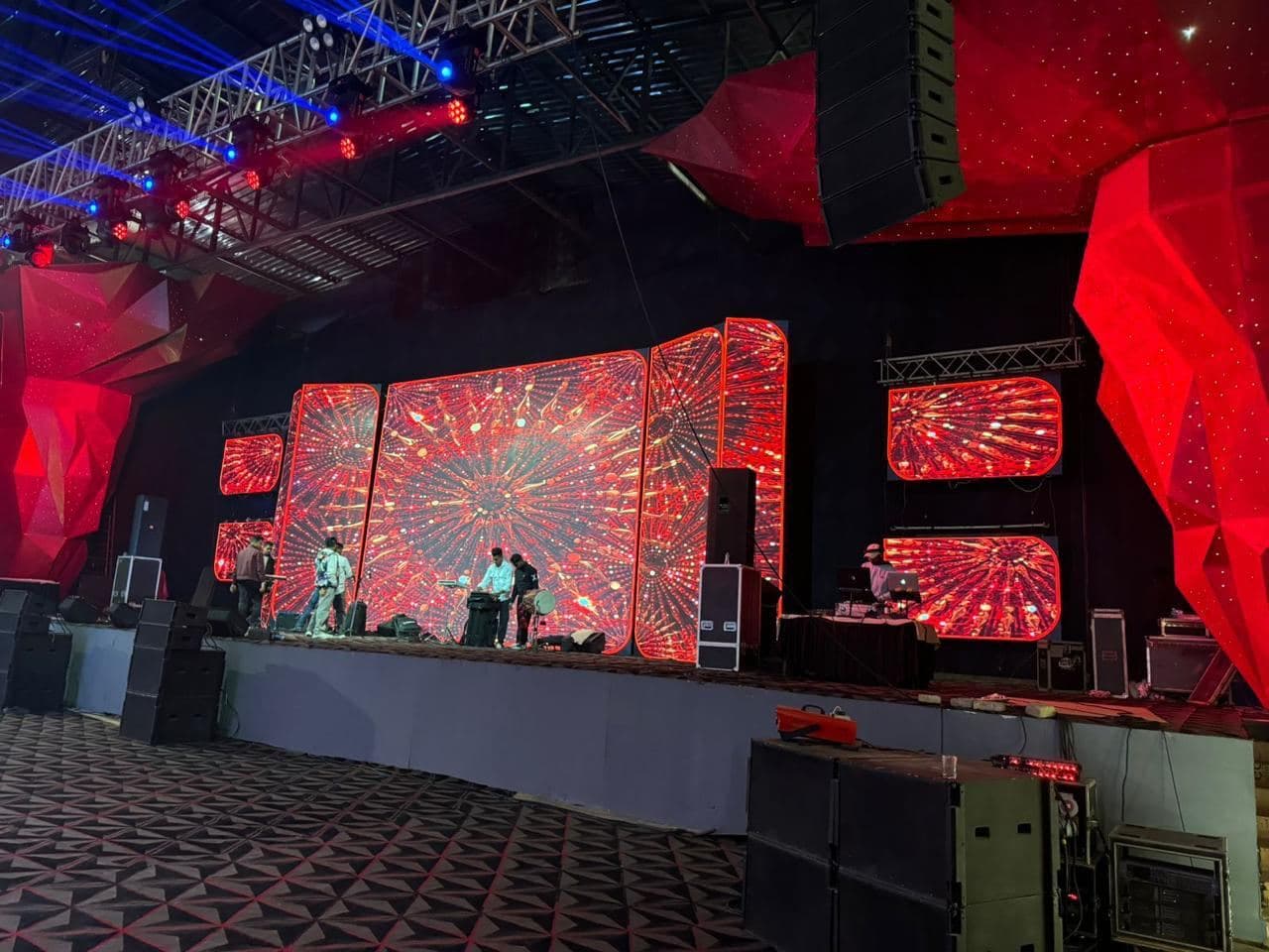 A large indoor LED video wall and side panels lit red above a truss-framed stage at a Siliguri function.