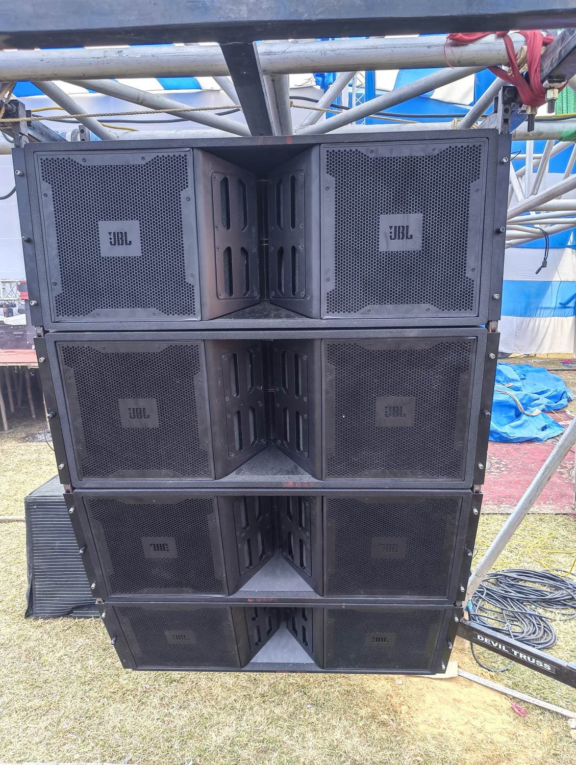 JBL line-array cabinets ground-stacked three high under truss on an open ground — gear we own and operate.