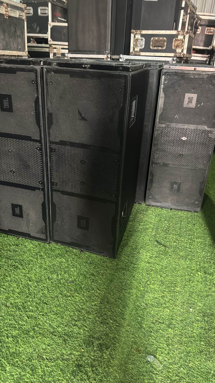JBL line-array boxes and subwoofers staged on turf beside flight cases before load-in