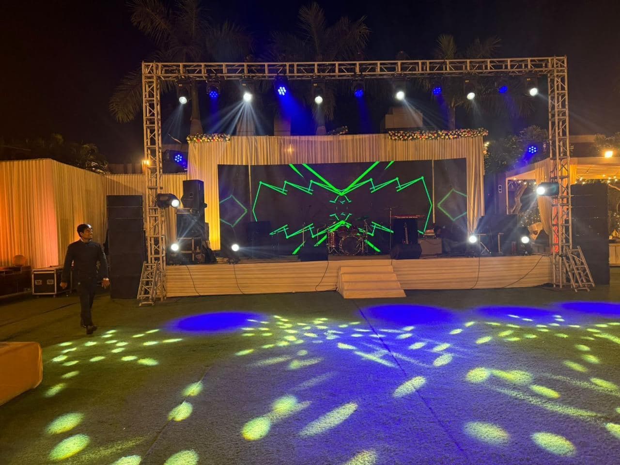 Moving-head gobos scattered across the dance floor in front of a truss-framed outdoor stage at night
