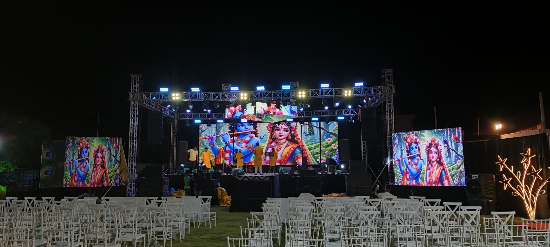 Outdoor night stage in North Bengal with a centre LED screen, two side LED panels and rows of guest chairs.